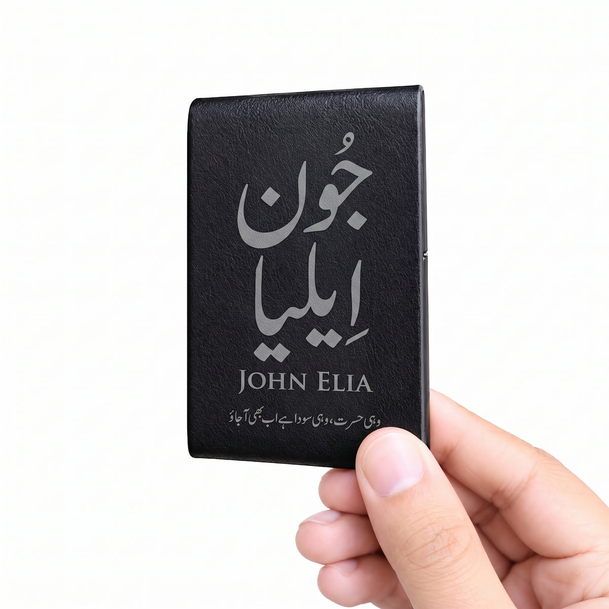 A hand holding a black leather card holder or wallet with silver Arabic and English text reading 'John Elia' on a plain white background.