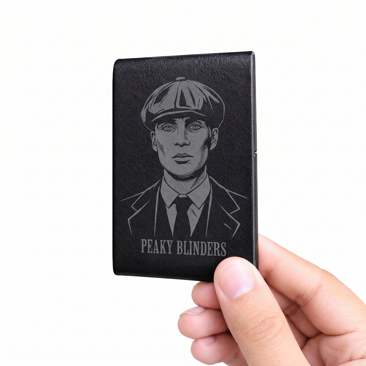 A hand holding a black leather card holder featuring an engraved portrait of Chucky from Peaky Blinders and the text 'PEAKY BLINDERS' on a plain white background.